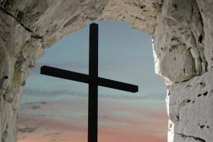 This photograph is taken from inside an empty cave, looking up into a blue sky and the outline of a cross.