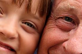This photograph shows a grandfather and a grandson cheek to cheek, looking straight ahead and smiling.  The focus is on their eyes.